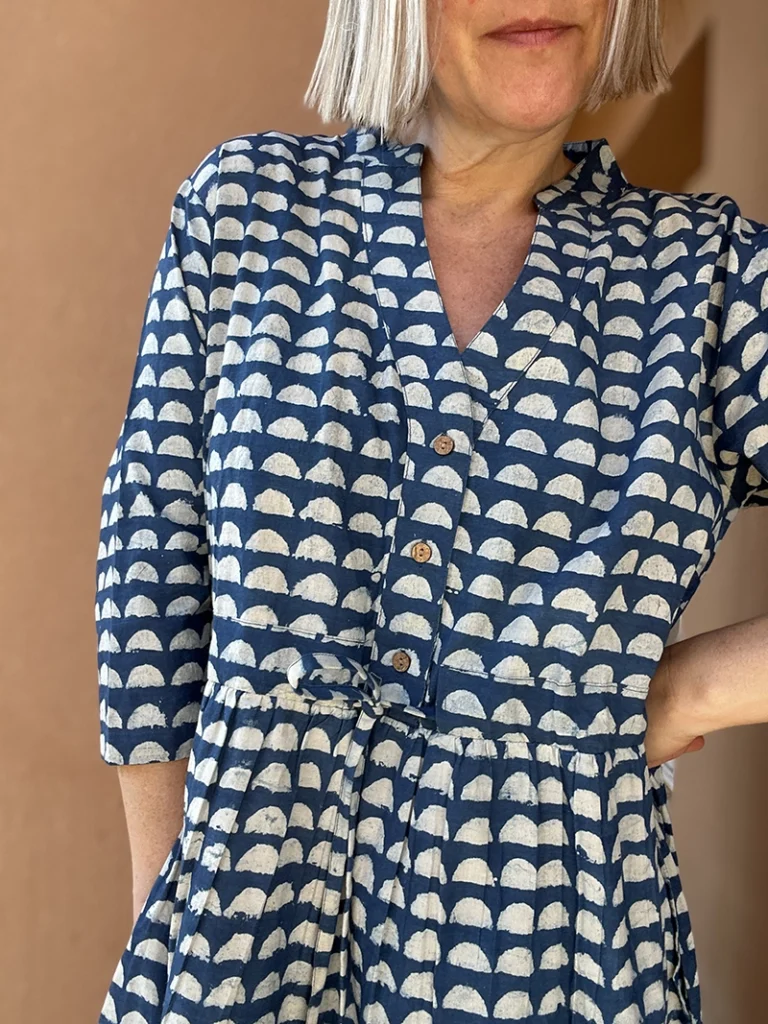 Woman wearing Roamni indigo Dabu block print button front dress with drawstring waist and side pockets.