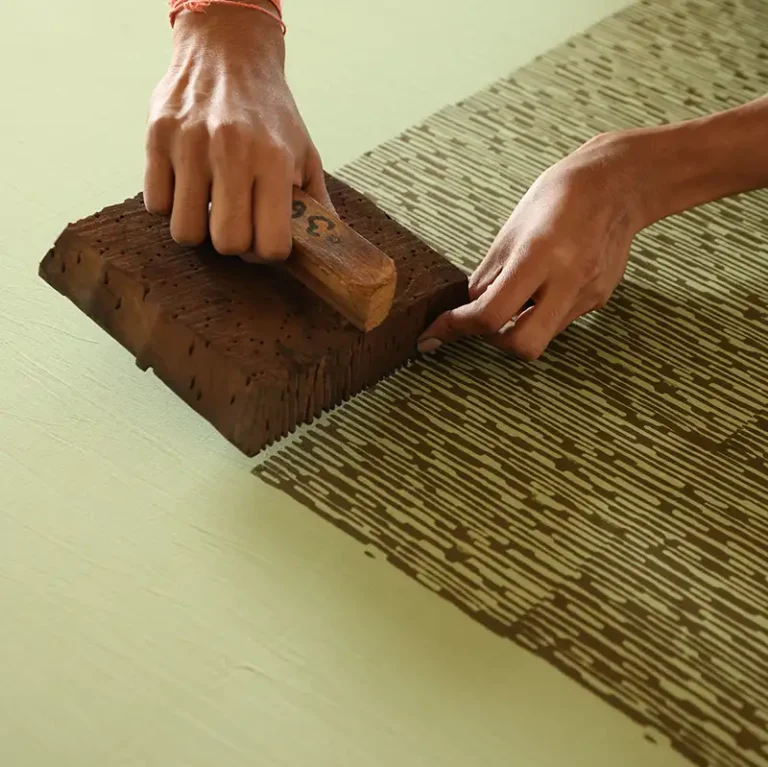 Close-up of artisan hands applying Sunray woodblock print to organic fabric in a Jaipur workshop.